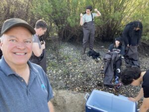 selfie of a mentor with students putting on waders on a rocky river bank near an open cooler